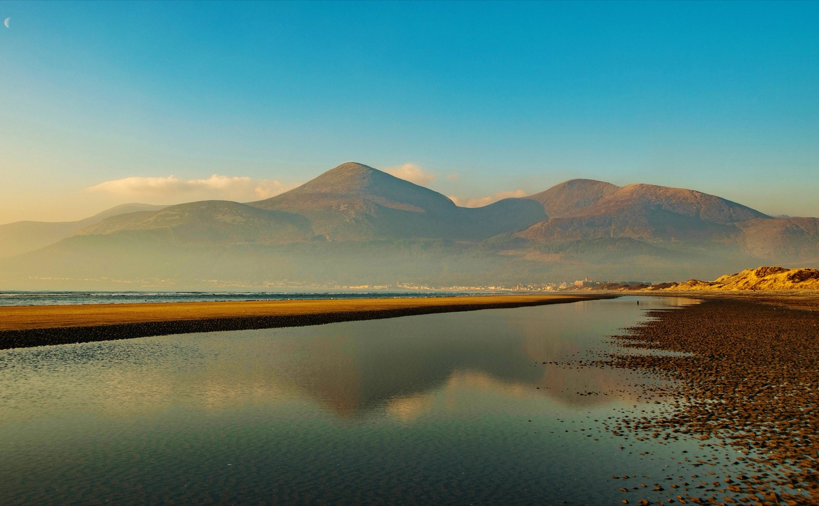 The long sandy beach at Newcastle at golden hour, with the Mourne Mountains and Slieve Donard sweeping down to the sea and reflected in the wet sand