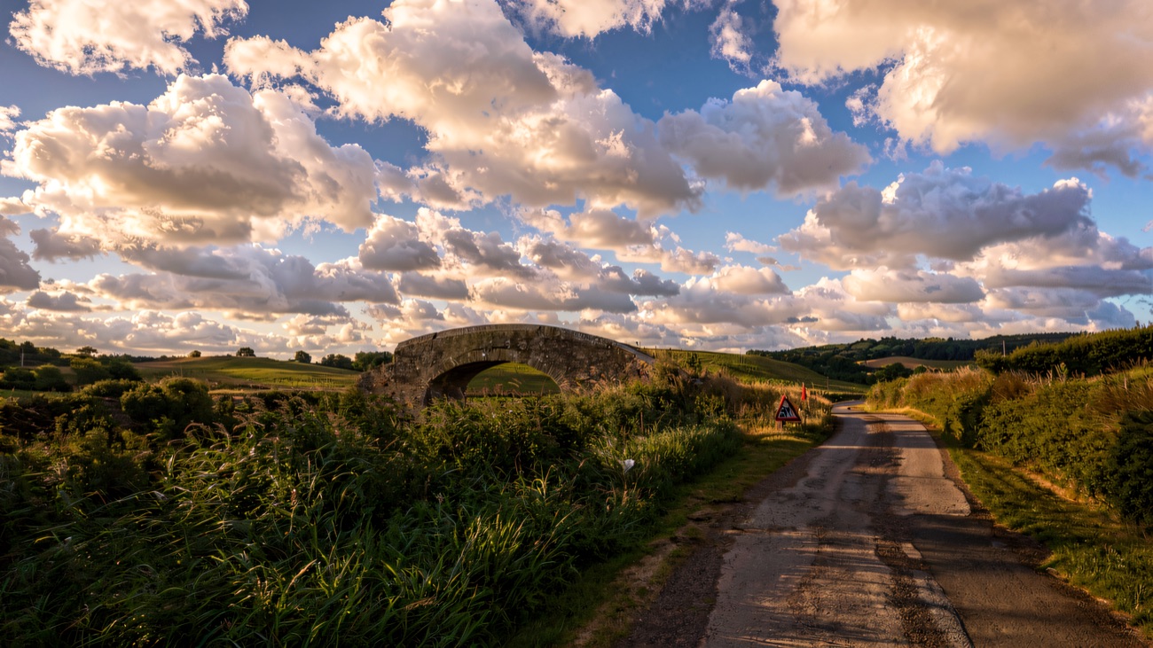 An old hump-back canal bridge sits in open farmland under a wide sky