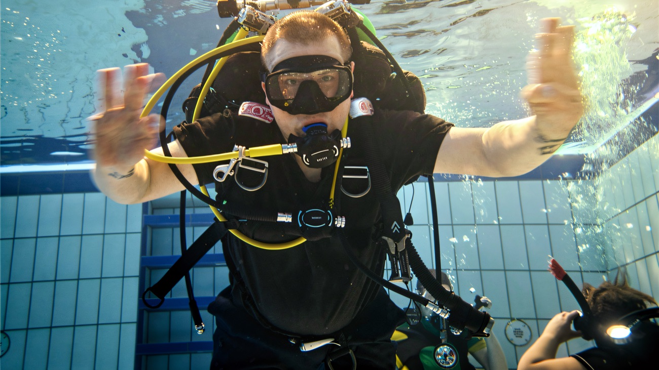 A diver in full scuba kit practising buoyancy at a club pool training session.