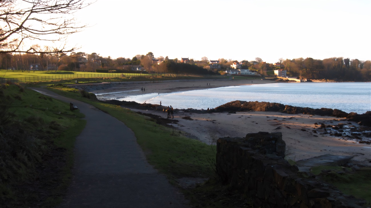 The paved coastal path curves along the water's edge toward the next bay.