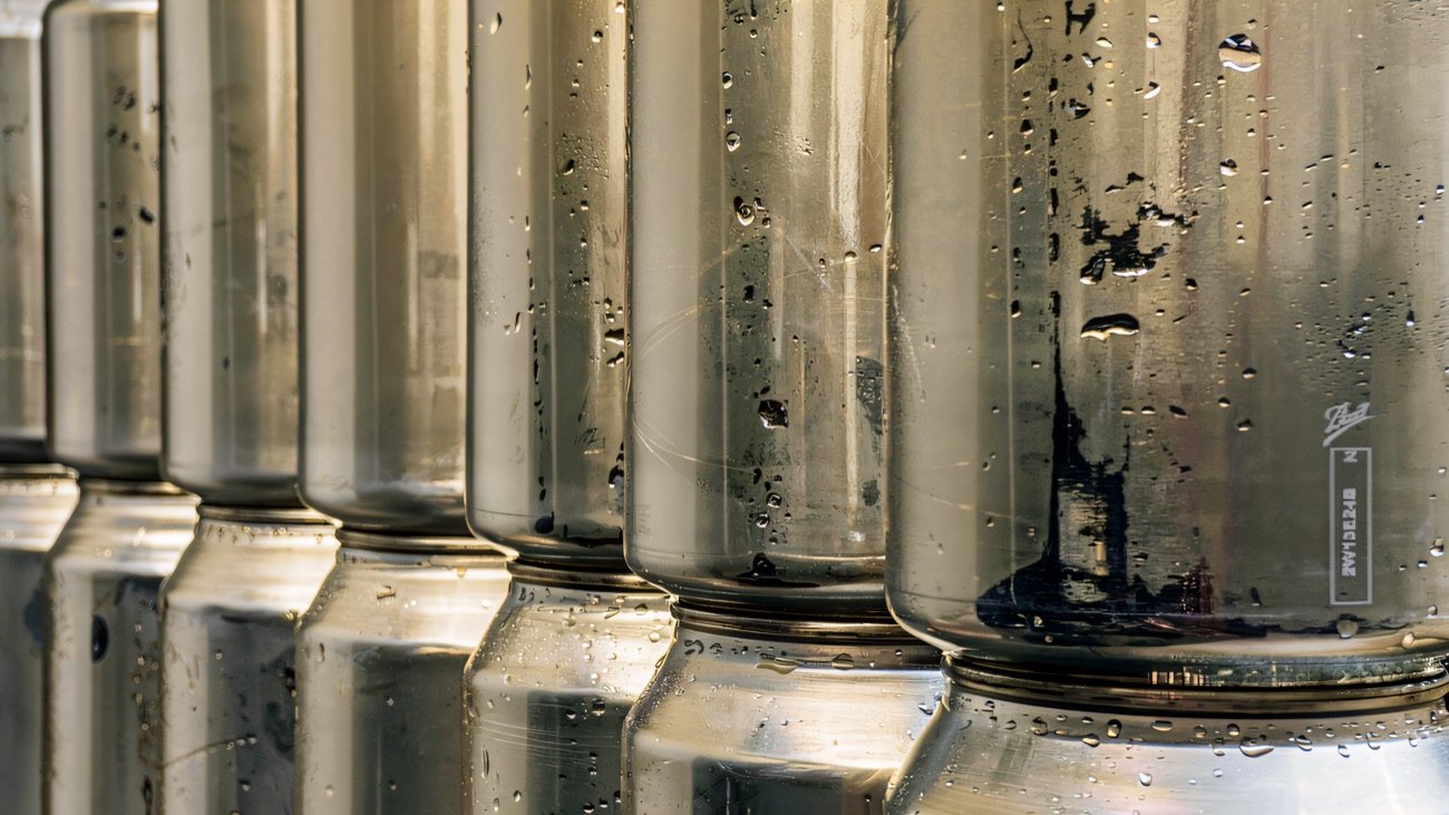 Rows of empty aluminium cans stacked and waiting to be filled, beaded with water in the packing area.