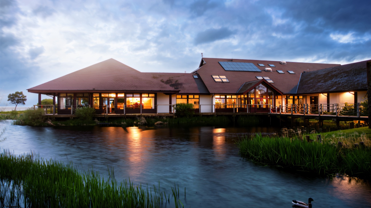 The Lough Neagh Discovery Centre reflected in the water at dusk, a duck gliding past