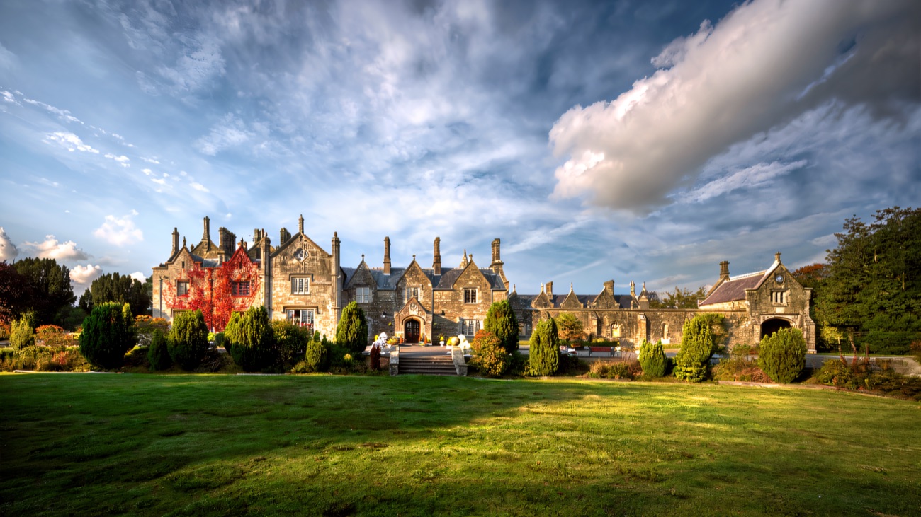 The front of Parkanaur Manor across a broad green lawn, its Gothic gables and chimneys behind clipped topiary and flower beds