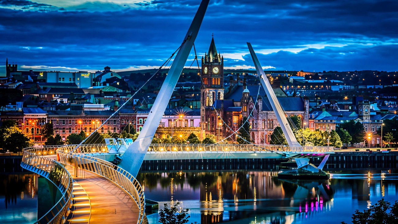 The Peace Bridge at blue hour with the illuminated Guildhall reflected in the calm River Foyle