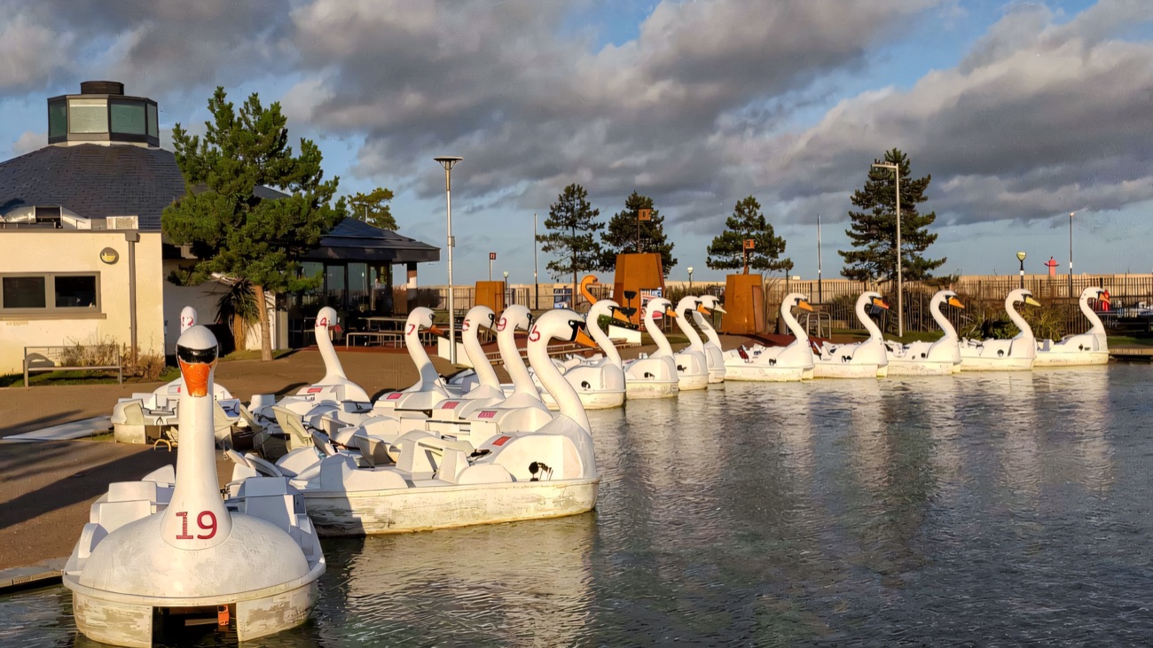 The white swan pedal boats lined up at the dockside under a dramatic Bangor sky