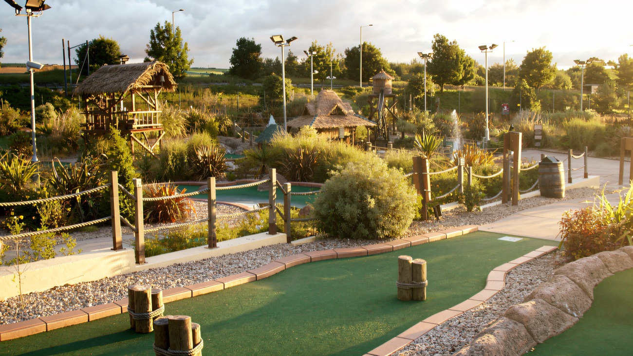 A wide view of the landscaped course with thatched huts, a lookout tower, rope-post greens and winding waterways