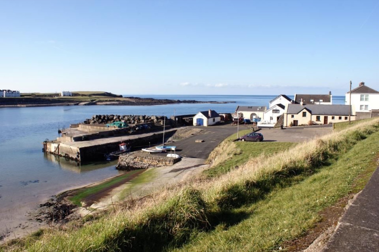 The small working harbour at Portballintrae with a slipway and boats under a bright blue sky