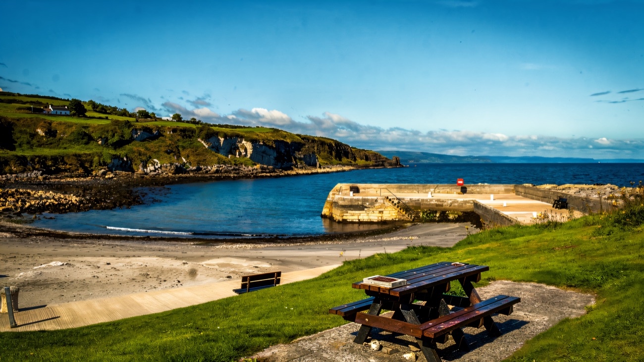 A picnic bench on the grass looking down over the empty beach, harbour wall and white cliffs