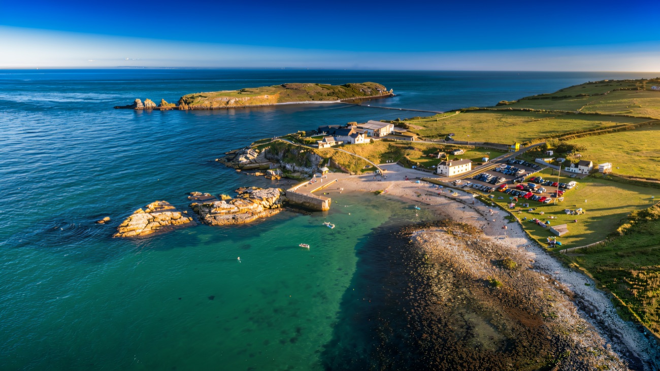 Aerial view of the harbour, clear green shallows and the green hump of the Isle of Muck offshore