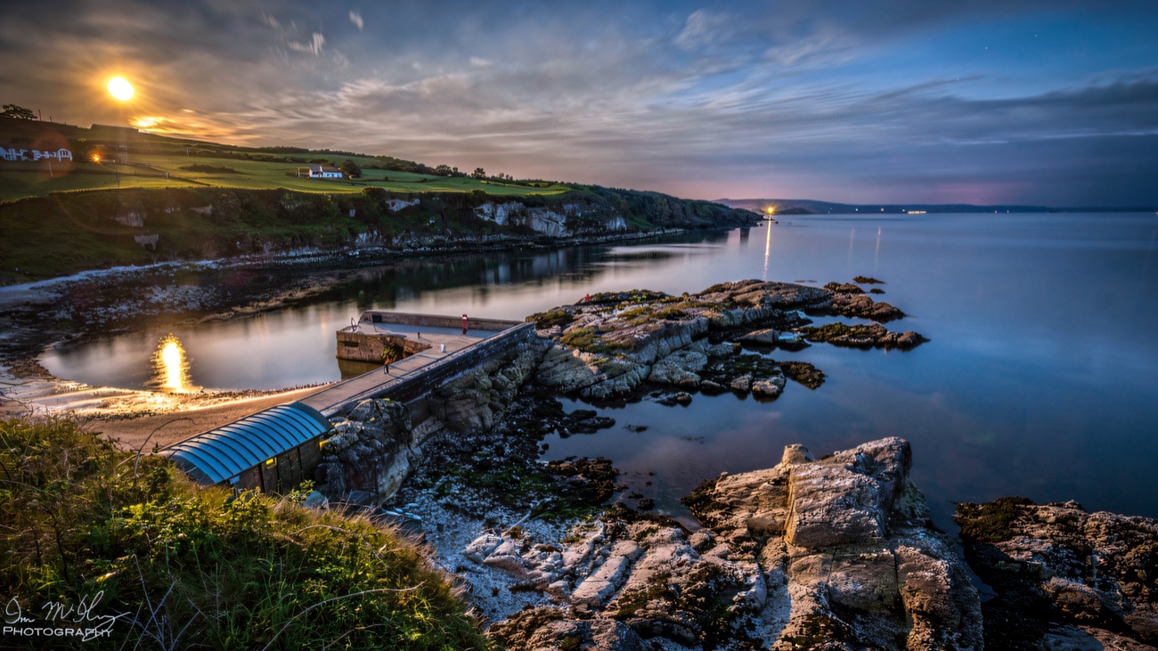 The harbour at dusk, still water reflecting the last light along the pier and shingle