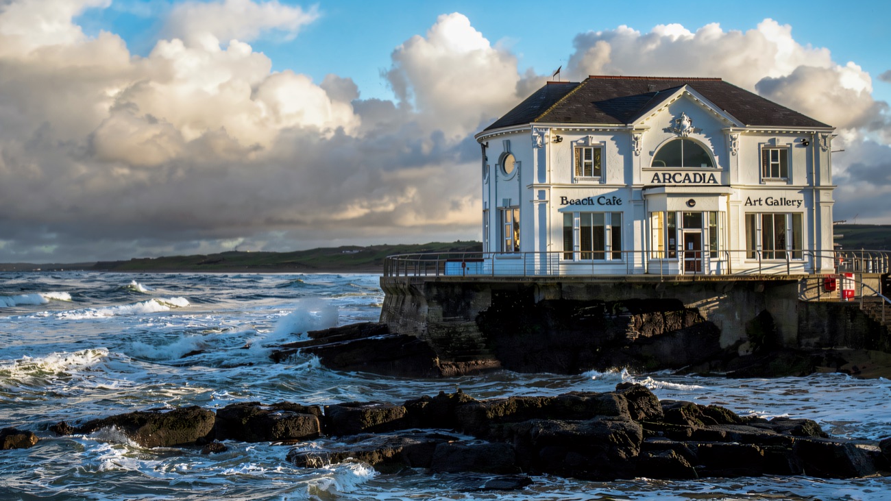 The Arcadia standing out on its rocky headland as the sea breaks white around the basalt shore.