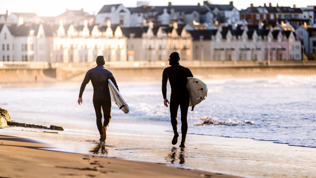 Boards under arm along West Strand, the seafront terraces catching the light