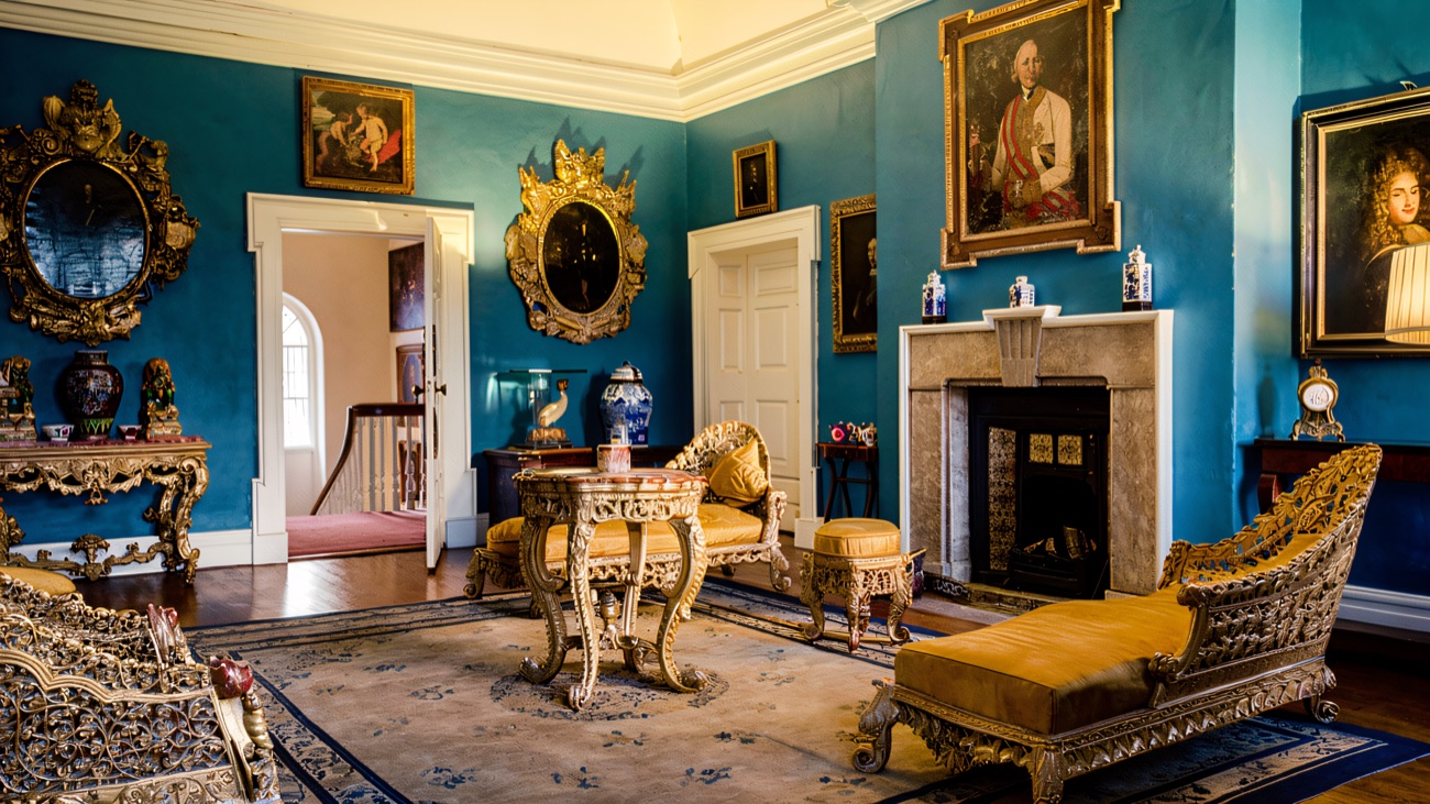 A grand teal-blue drawing room inside Prehen House with gilt furniture, portraits and a marble fireplace