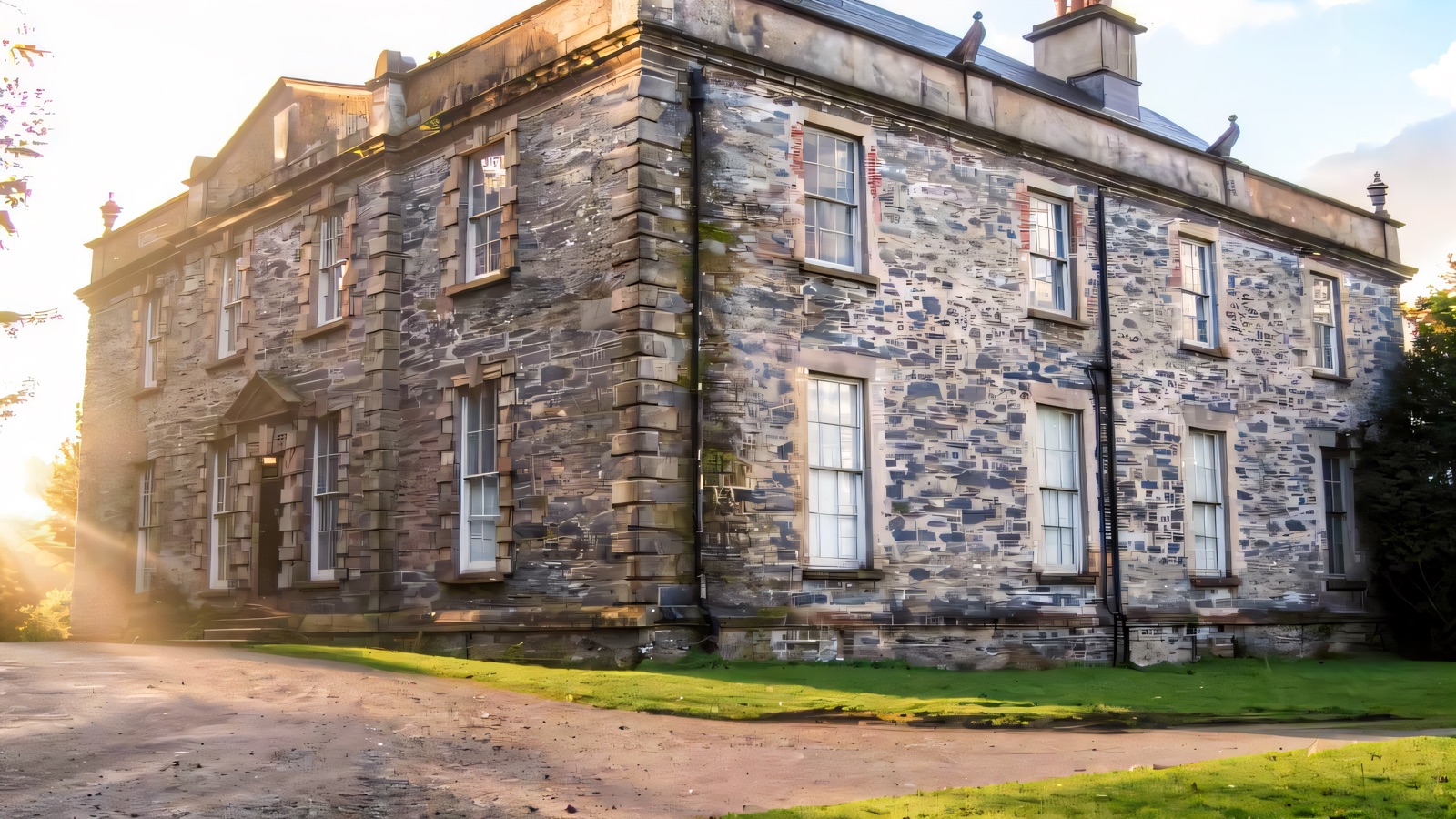 The grey stone Georgian front of Prehen House seen from the corner, with sash windows and a lawn