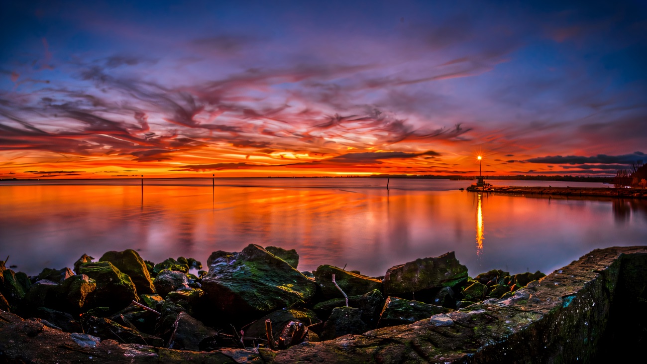 Sunset over a wide lough, with orange and purple sky reflected in flat calm water above a rocky shore
