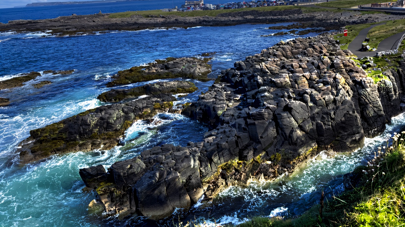 Black rocks and turquoise surf at the point, Portrush along the shore