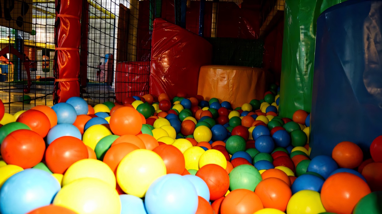 A deep ball pit filled with red, blue, yellow and green balls beside the padded play frame