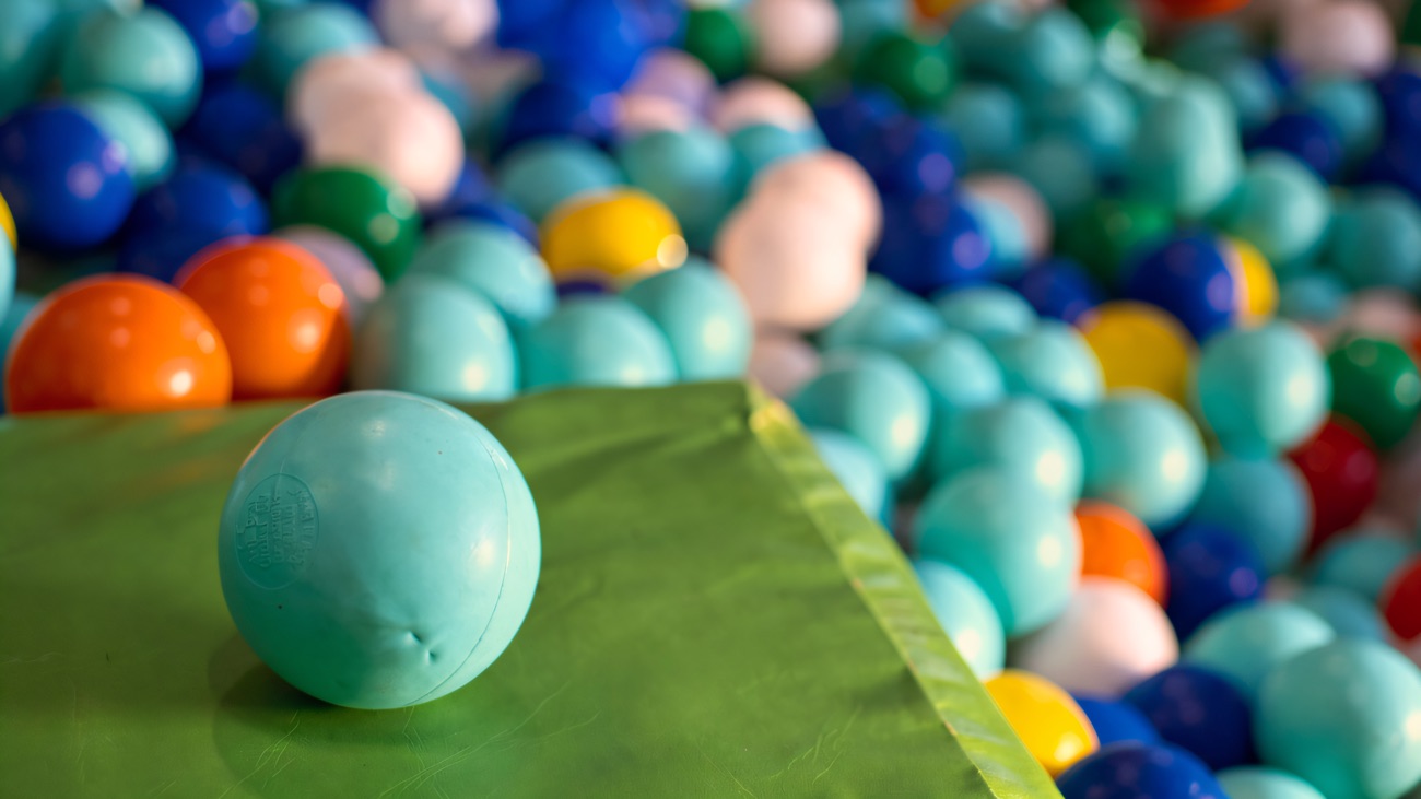 A close view of the ball pit, mint and blue balls spilling over a green padded edge