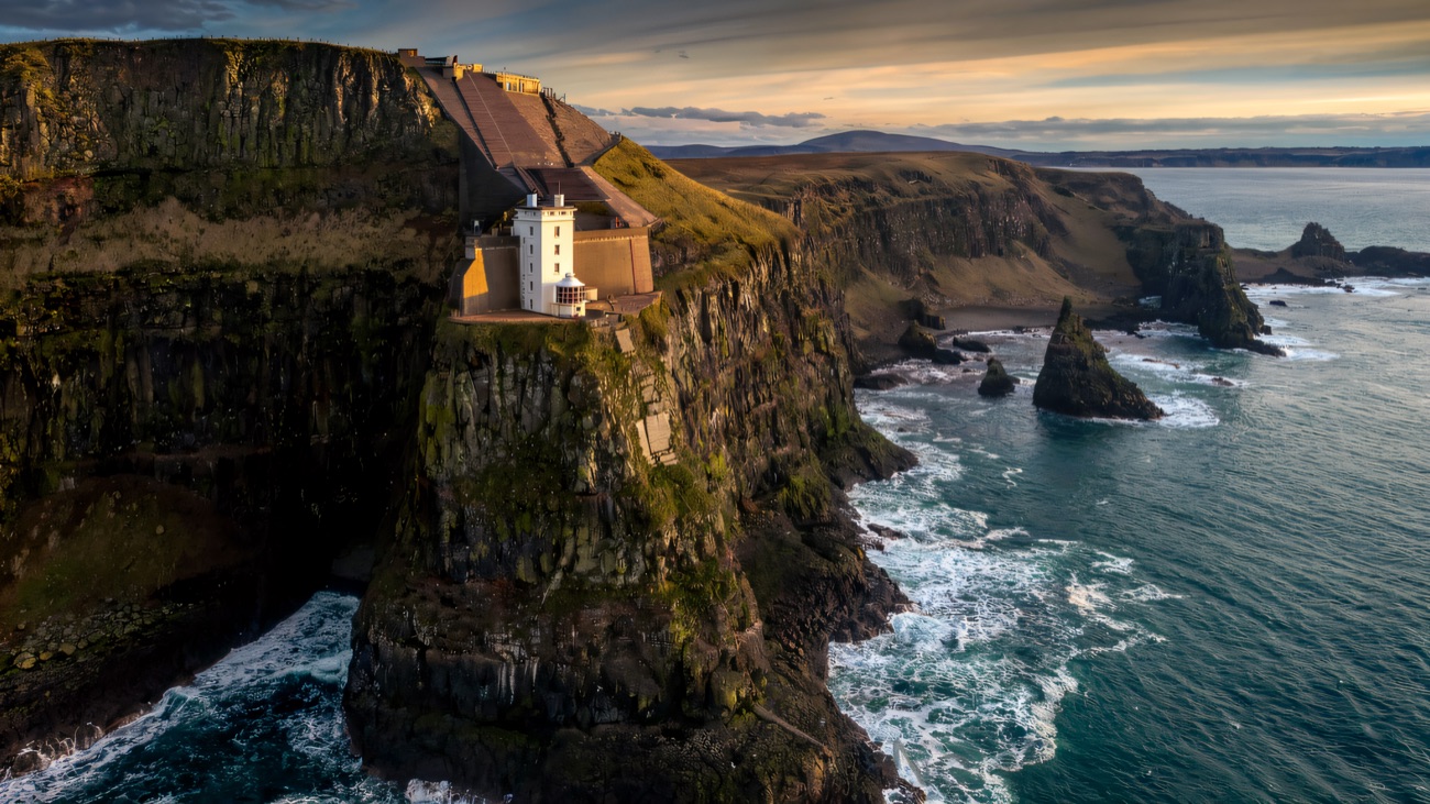 The lighthouse and cliffs in soft evening light, surf working the rocks far below.