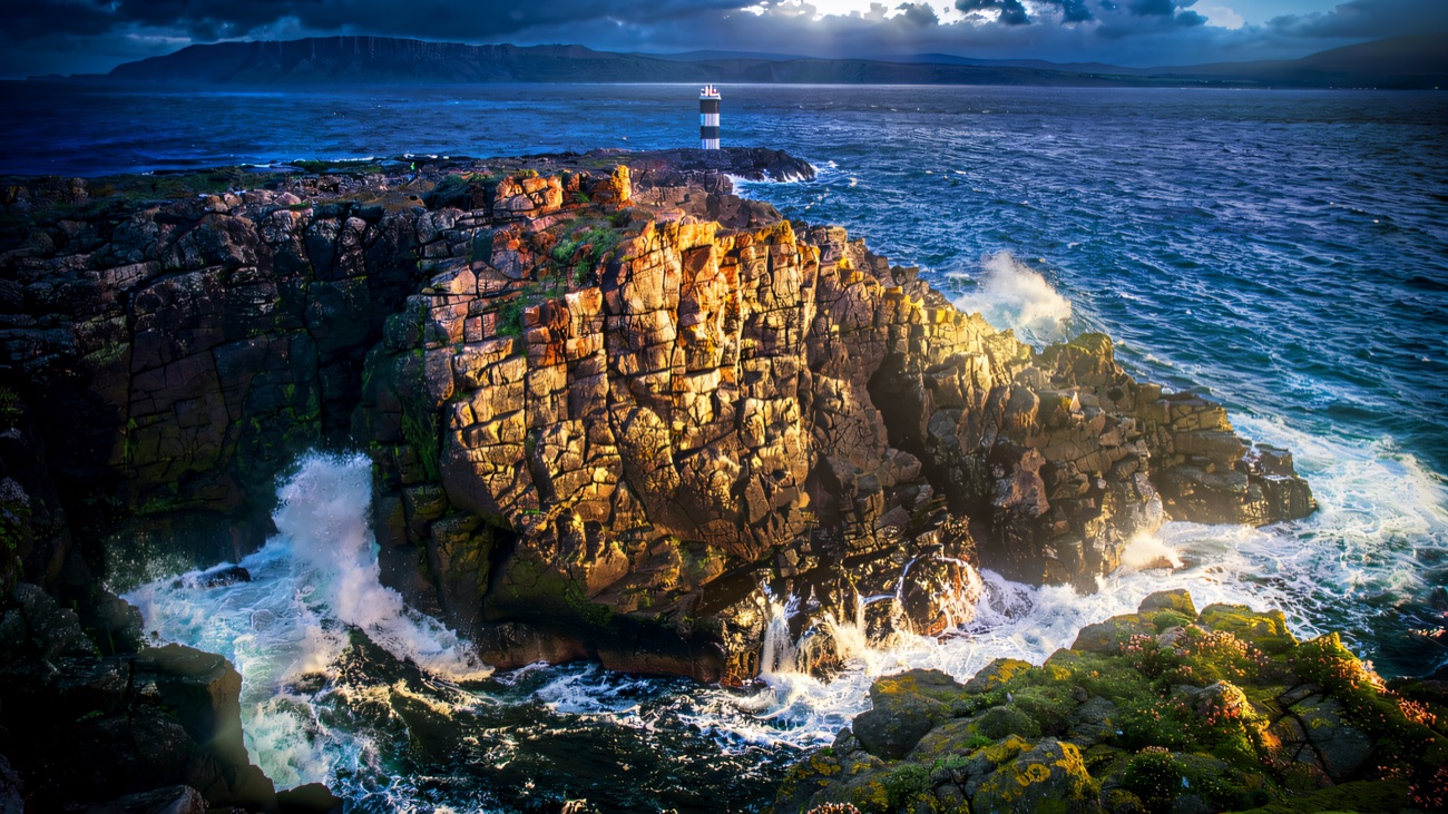 A lighthouse standing over the rocks as the waves roll in