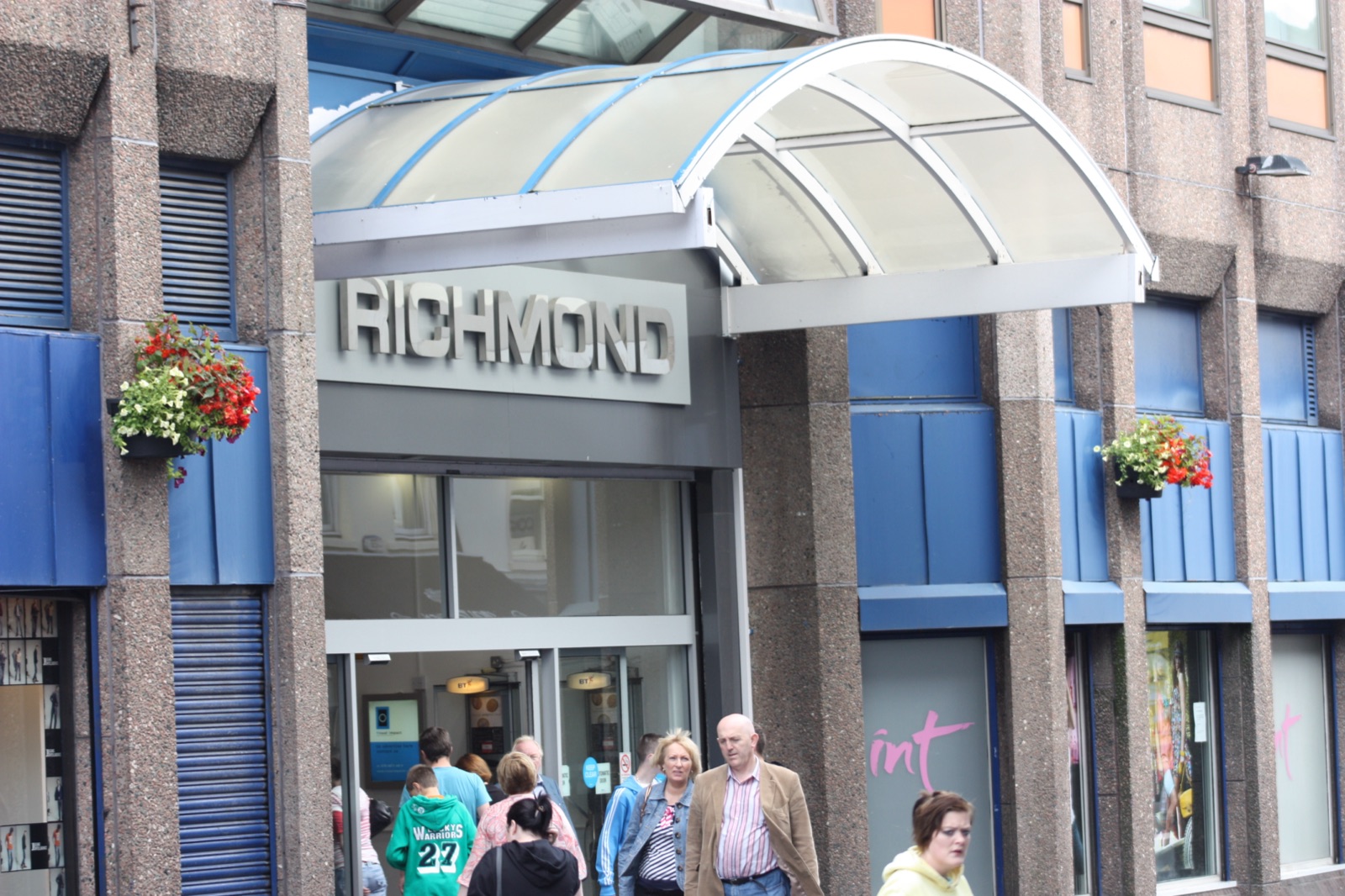 The curved glass canopy over the RICHMOND entrance on Ferryquay Street, Derry, with shoppers passing below