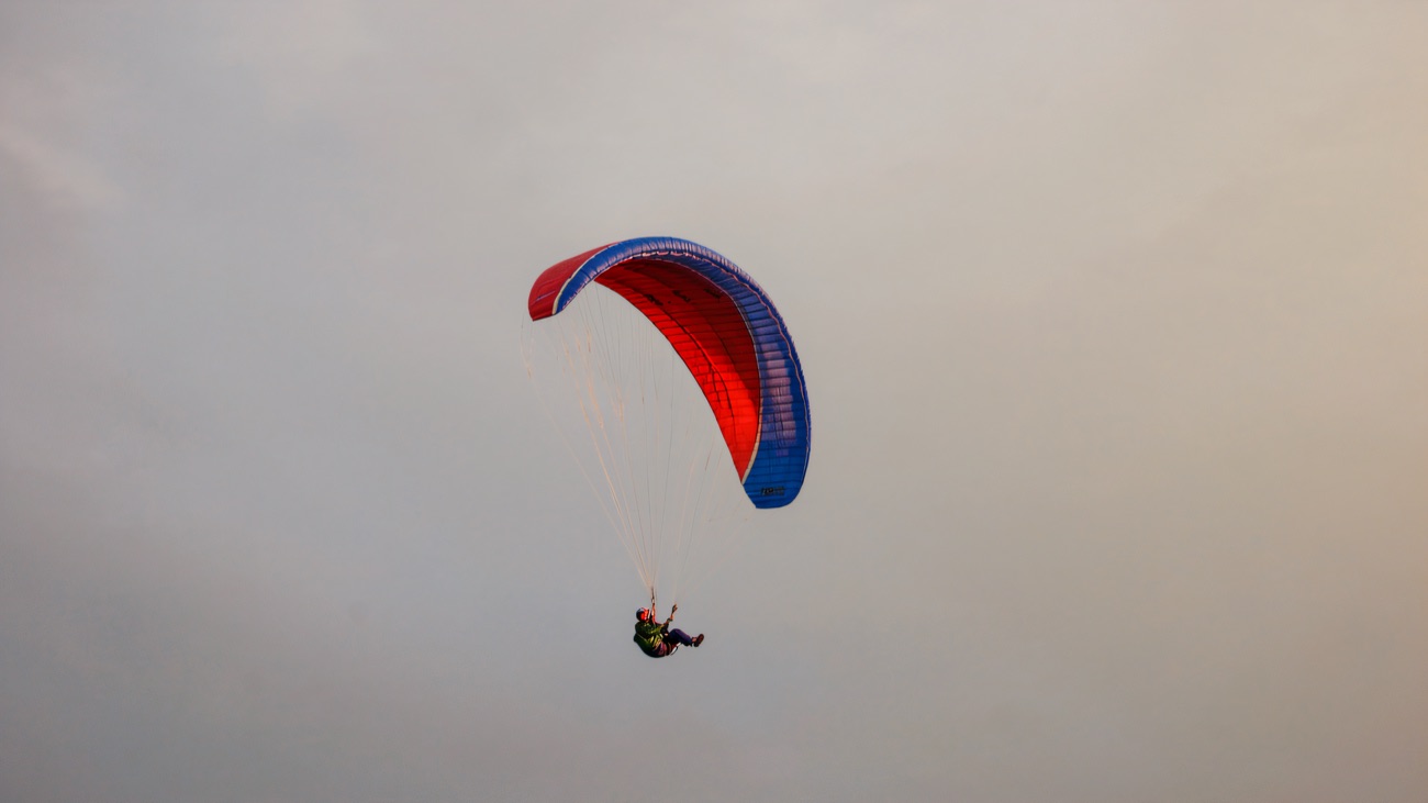 A red and blue paraglider wing turning in a soft grey sky
