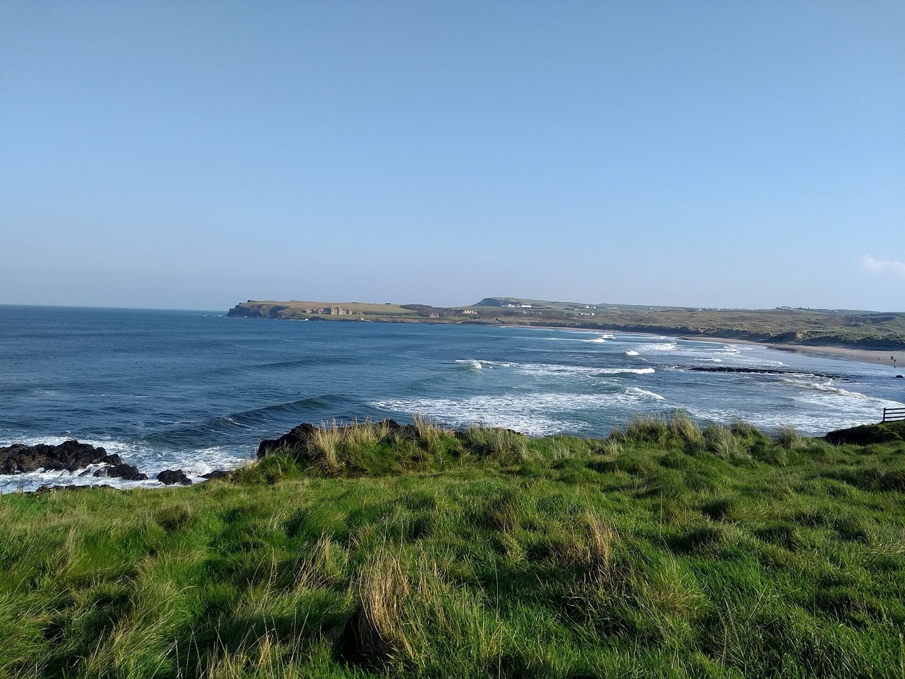 Elevated view along the long curve of Runkerry Strand, white surf and golden sand backed by dunes and the Runkerry headland