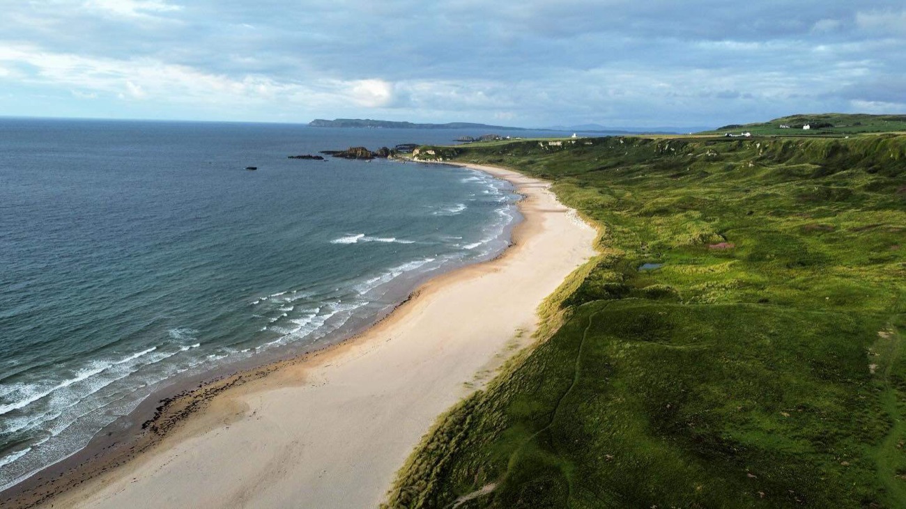 Aerial view of the golden curve of Runkerry Strand meeting dunes and green Causeway Coast headland