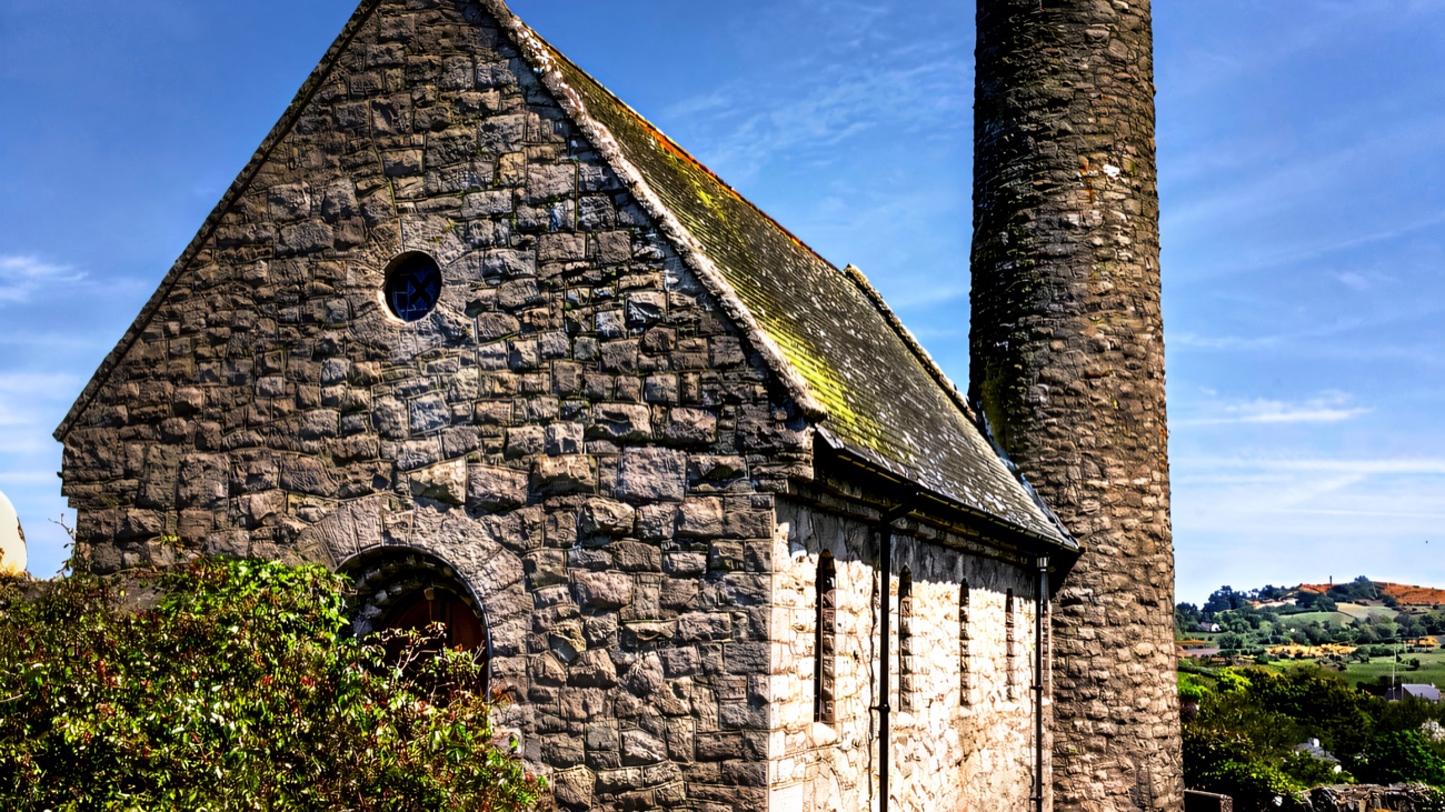 A closer view of the stout stone church and its slender round tower under blue sky.