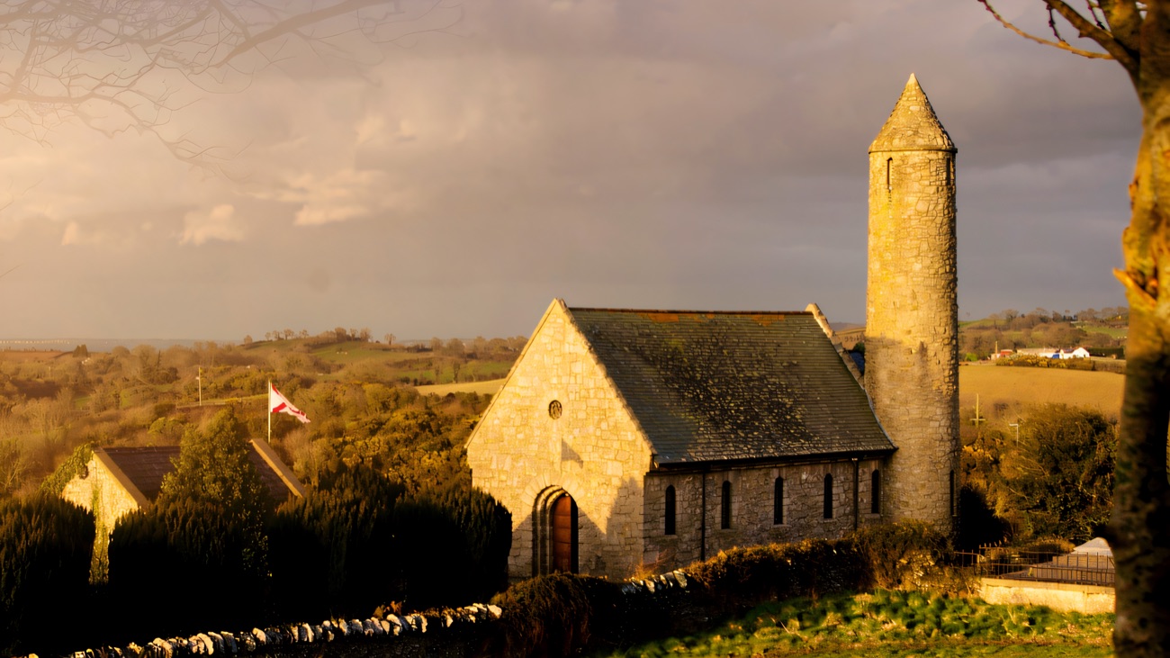 Dramatic golden storm-light breaks over the church and tower on their drumlin hilltop.