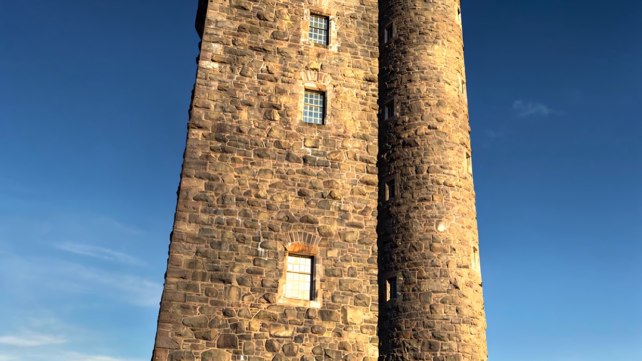 A low-angle close-up of Scrabo Tower's turreted stonework against a blue sky