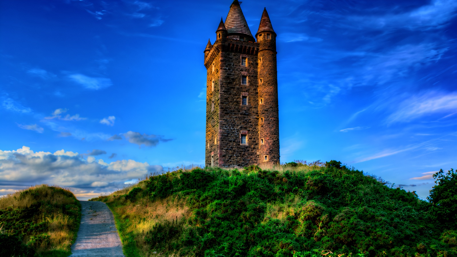 Scrabo Tower, a tall stone tower on its green hilltop with a path leading up under a blue sky