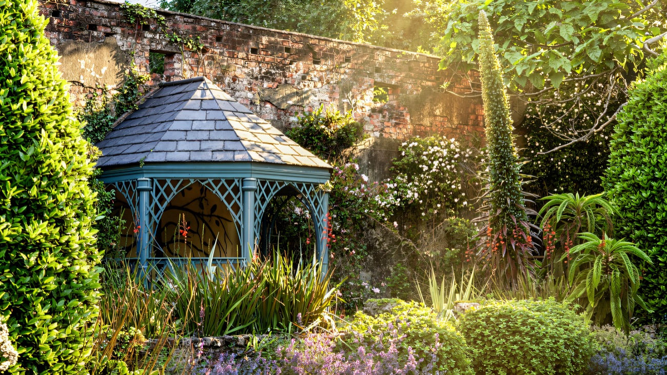 A blue-painted wooden gazebo in a walled border of lavender and crocosmia in the historic garden