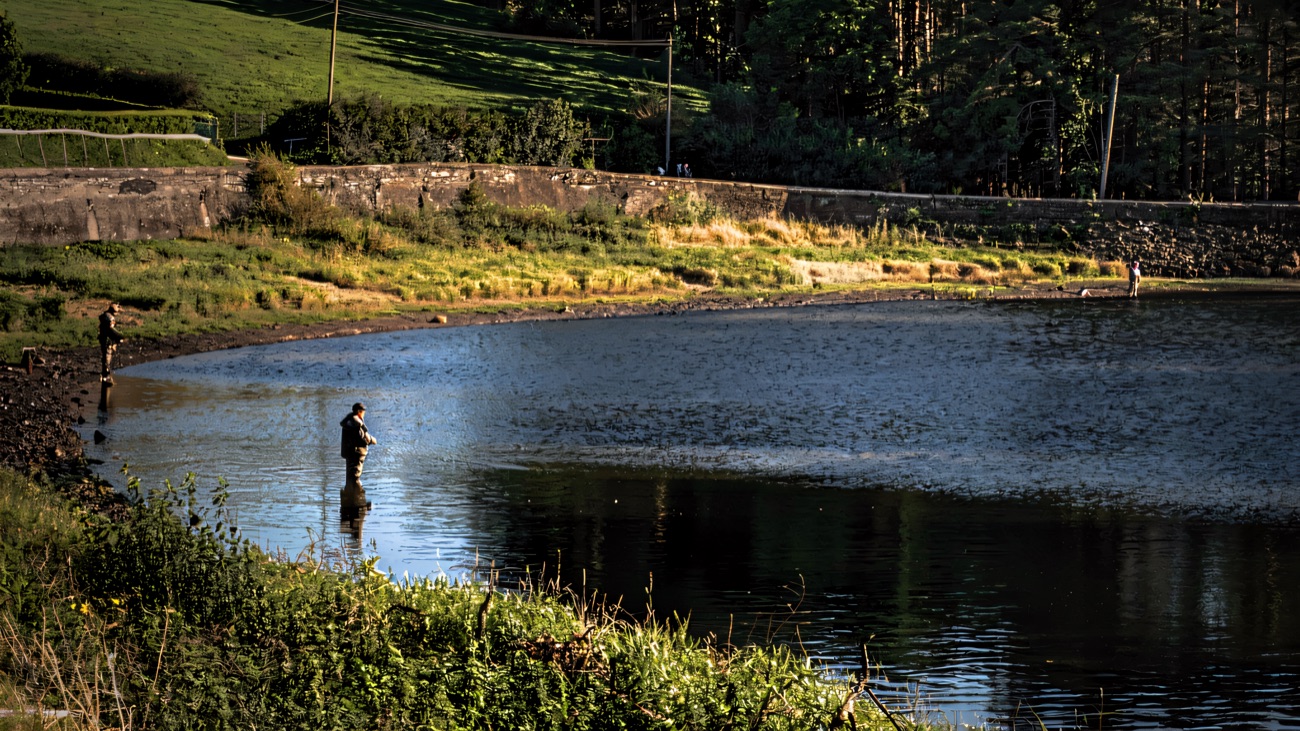 Anglers wading the lake below the green hillside