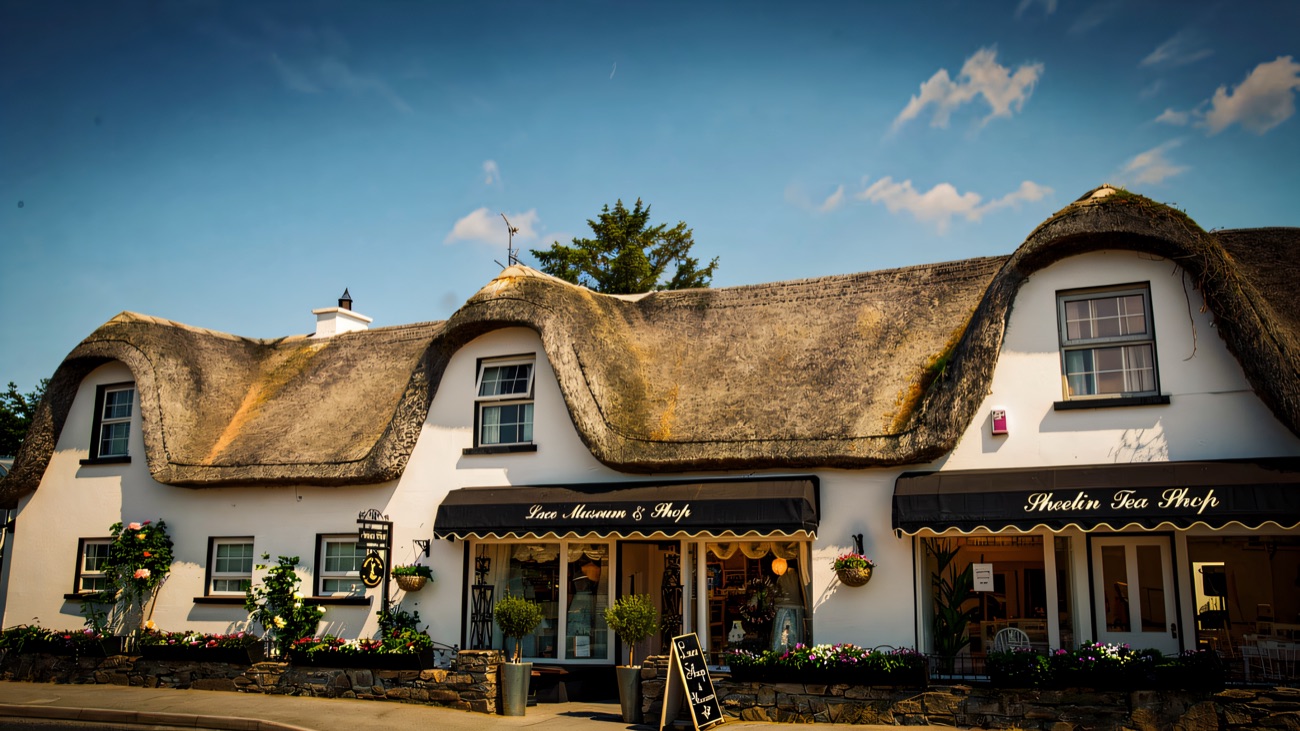 The white thatched building on the roadside, with the tea shop and lace museum awnings and flower boxes along the front.