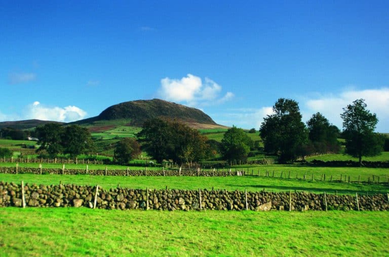 Layered dry-stone walls and green fields running up to Slemish mountain under a big cloudy sky