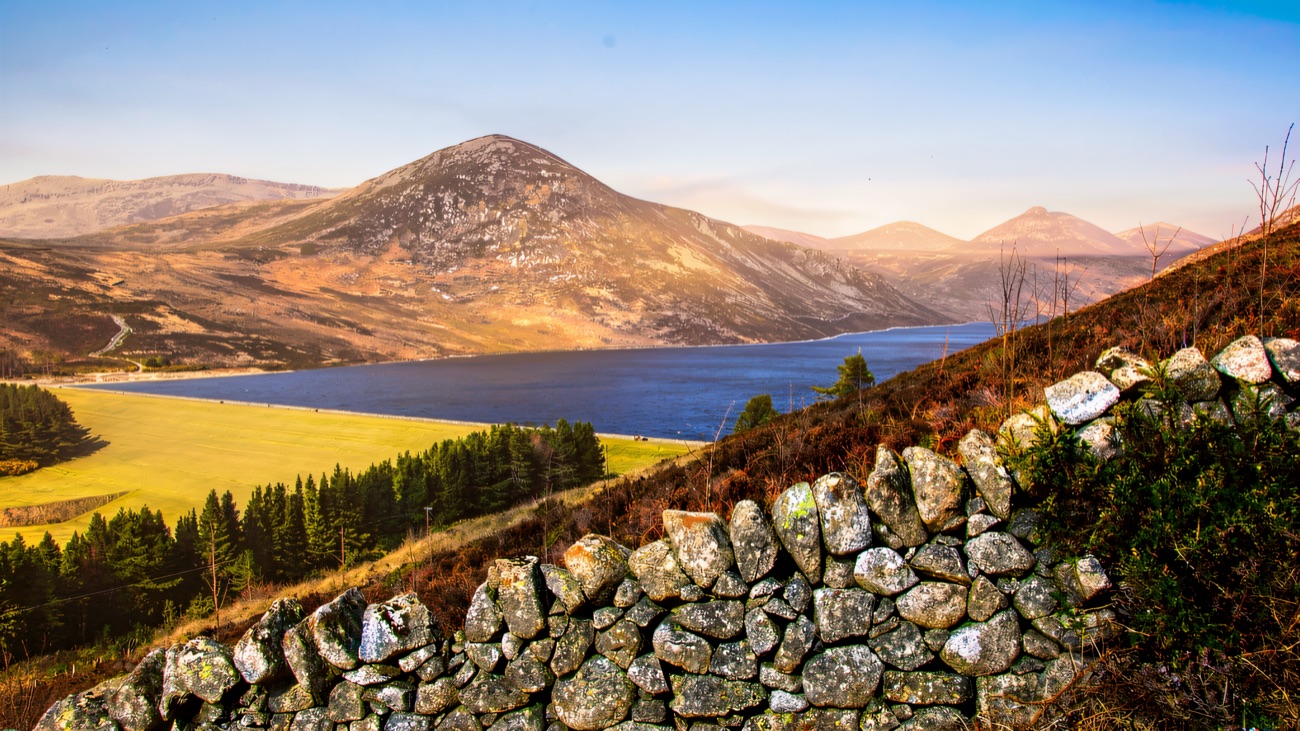 A dry-stone wall runs down to the water with the peaks rolling behind