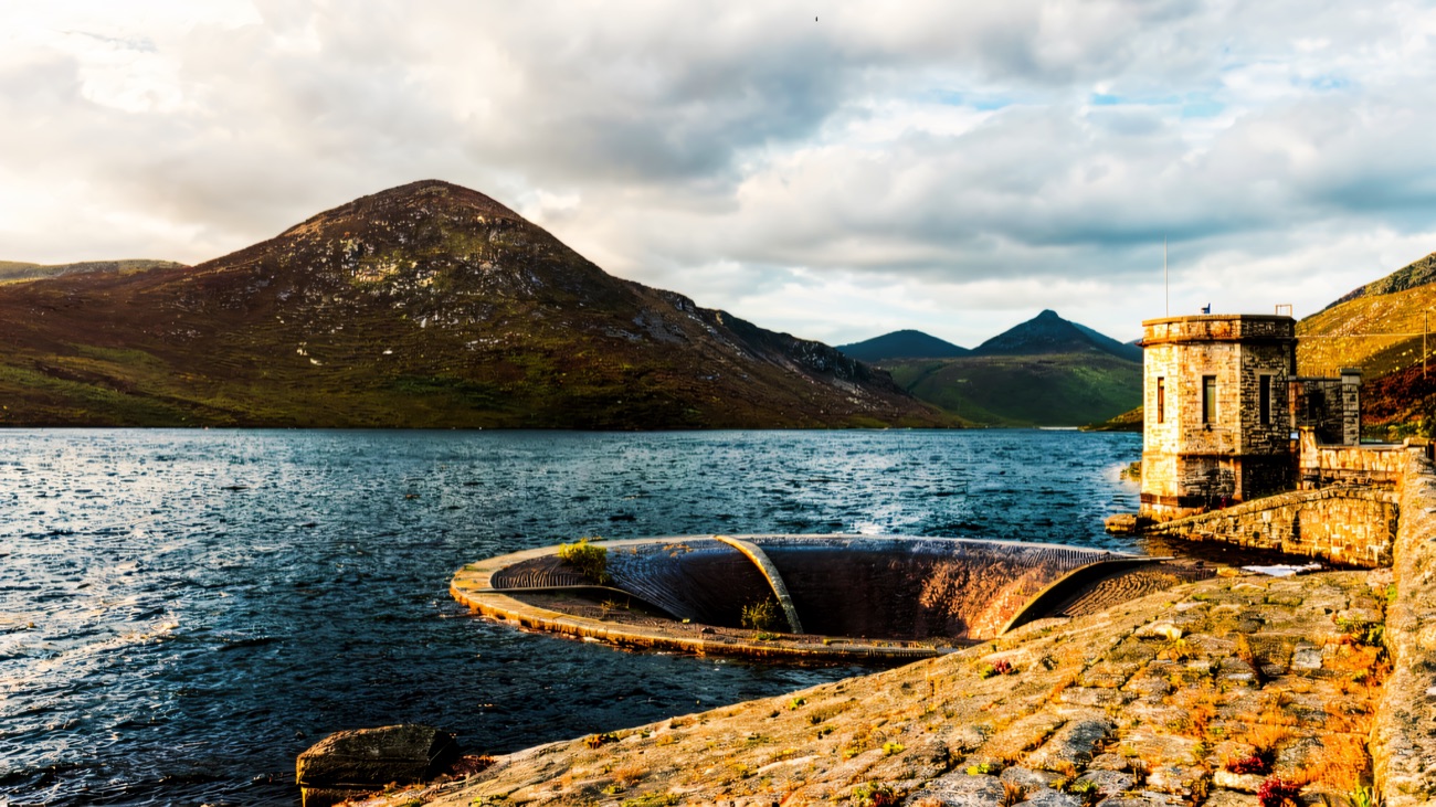 The Silent Valley reservoir with the bellmouth spillway and the Mourne peaks rising beyond under a cloudy sky