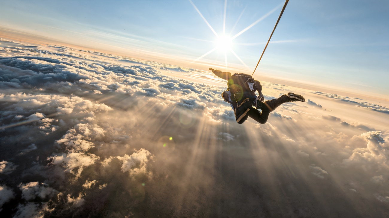 A jumper falling away under the sun with a blanket of cloud stretching to the horizon