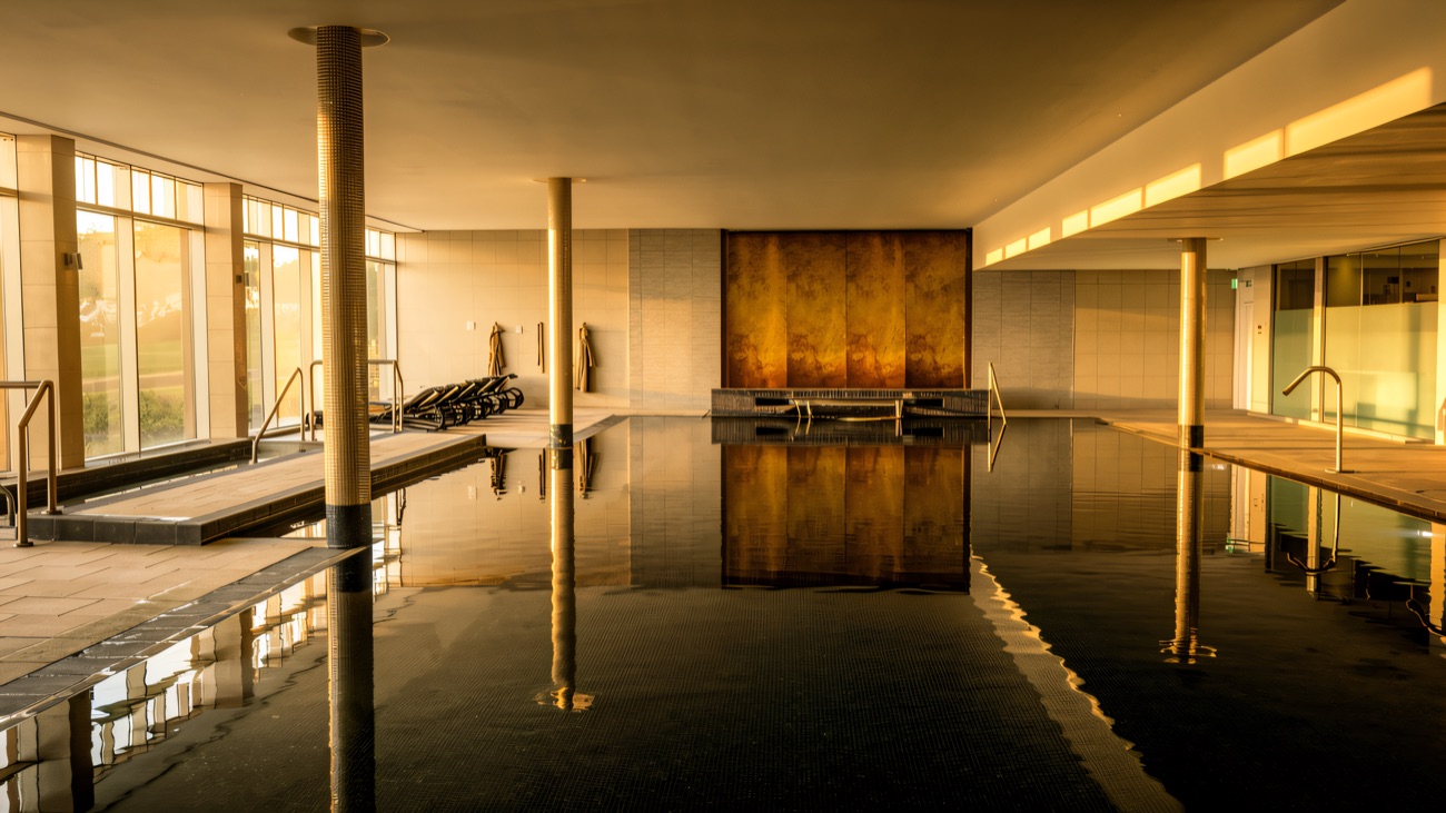 The still indoor pool with a warm gold feature wall and a wall of glass to one side.