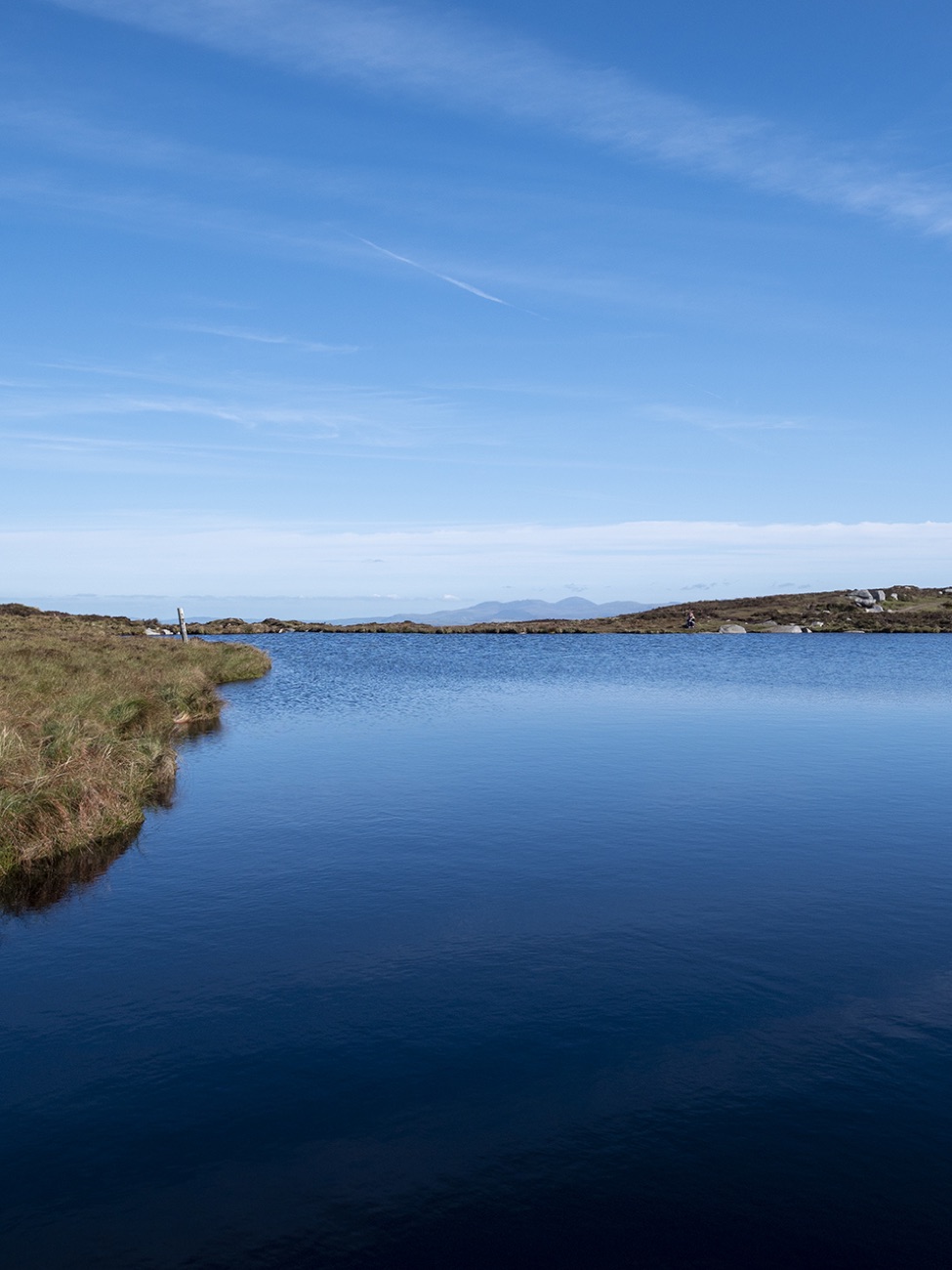 Calliagh Berra's Lough, a small blue lake on the mountain top under a blue sky.
