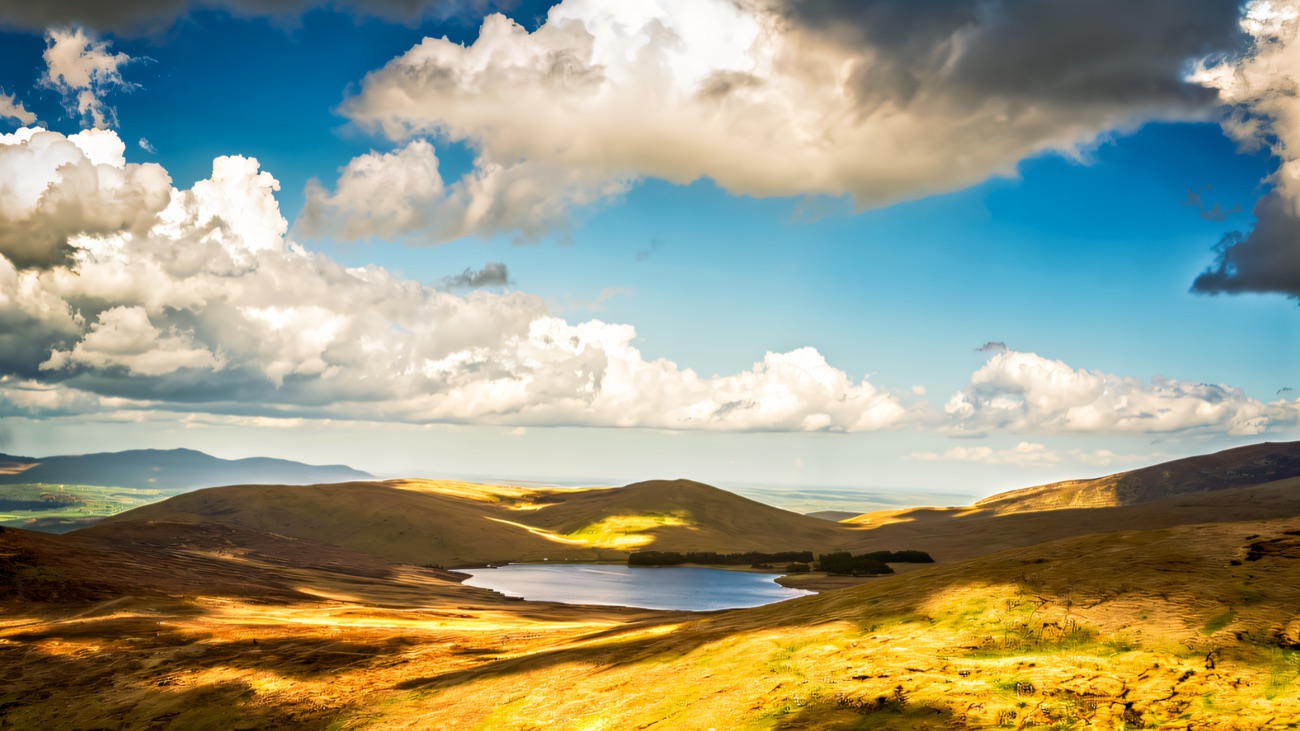 Spelga Dam sitting in a bowl of golden Mourne hillside under big summer clouds