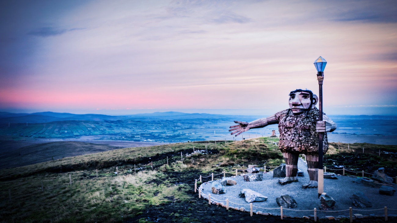 Darach silhouetted at sunset, arm sweeping across the wide Sperrin vista.