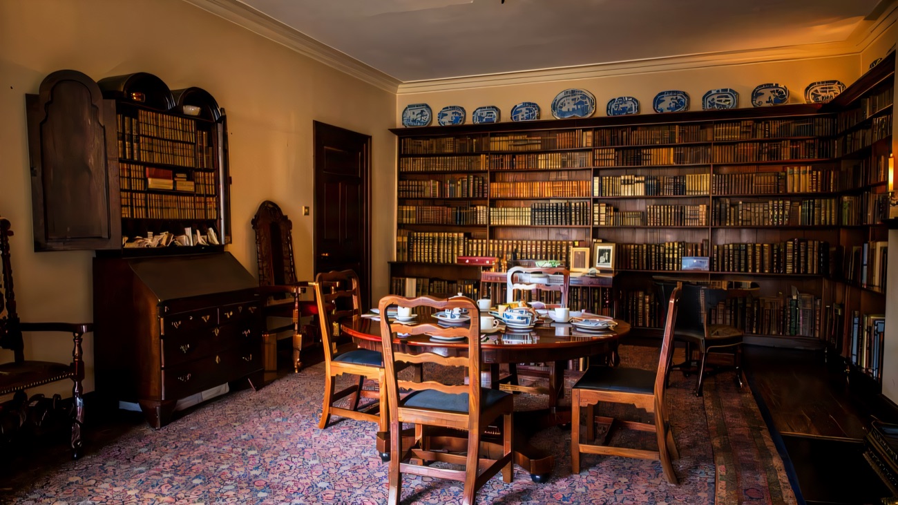 A wood-panelled room inside Springhill lined with shelves of leather-bound books and a round table set with blue-and-white china