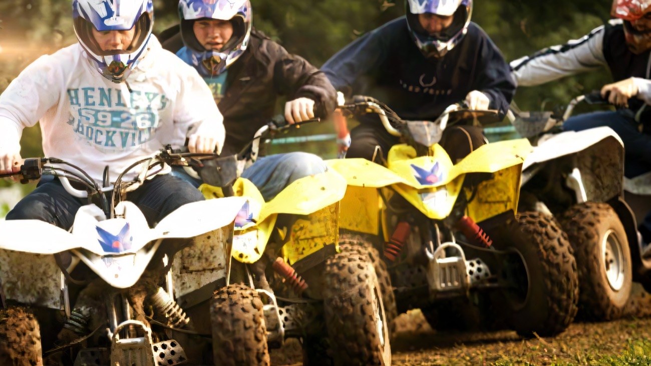 Helmeted riders racing quad bikes across a muddy grass field