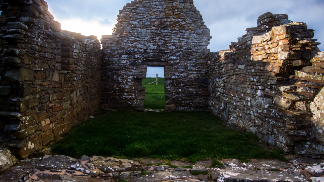 Inside the roofless church, looking down the grassy nave to the doorway in the gable.
