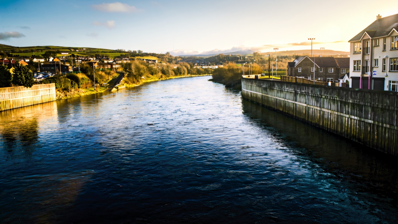 The River Mourne widening past the riverside walkway with hills beyond