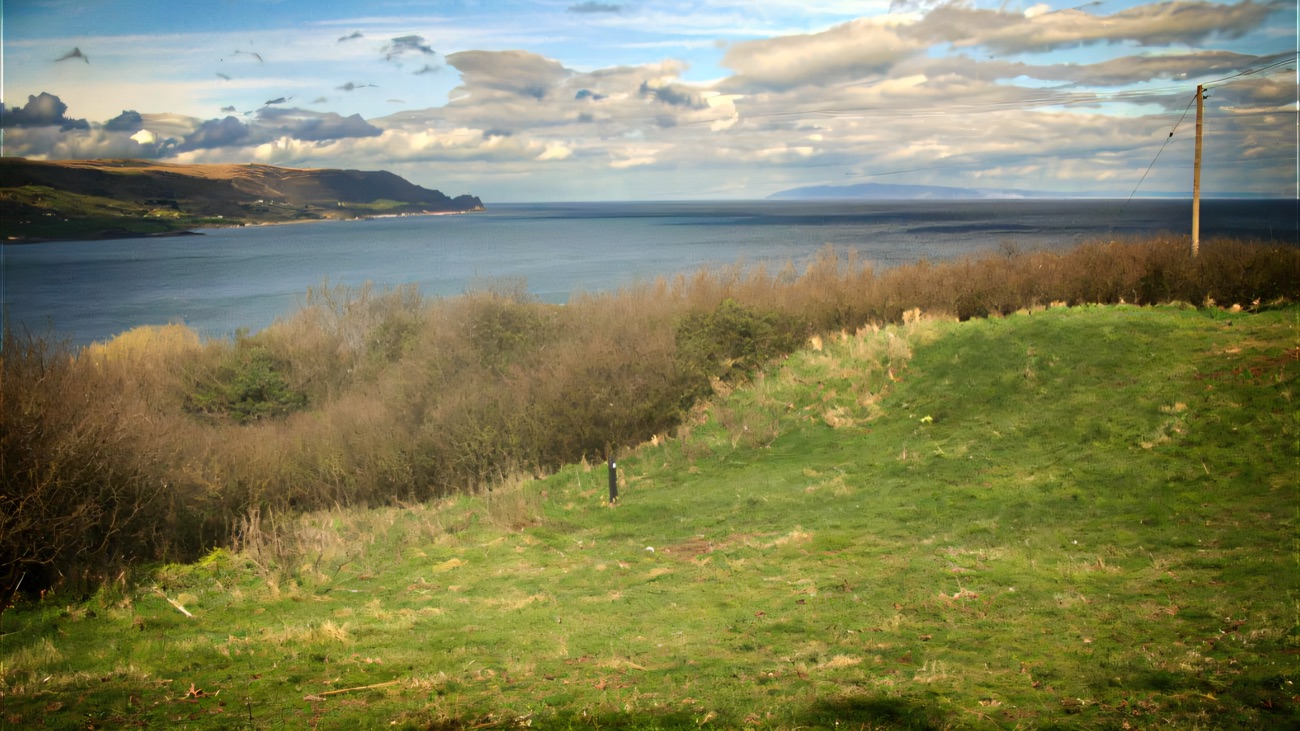 A grassy clearing opening to a broad sweep of sea toward the headlands beyond.