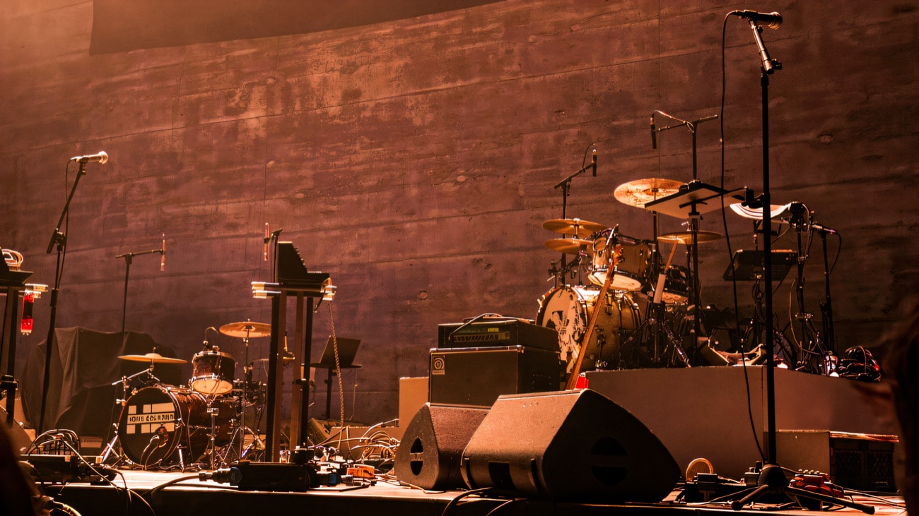 An empty stage set up with drums and mics against bare concrete