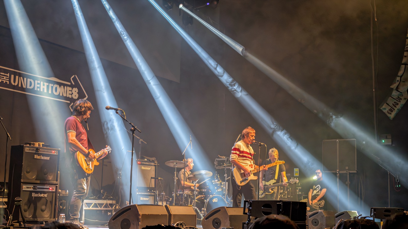 A band playing under beams of white light